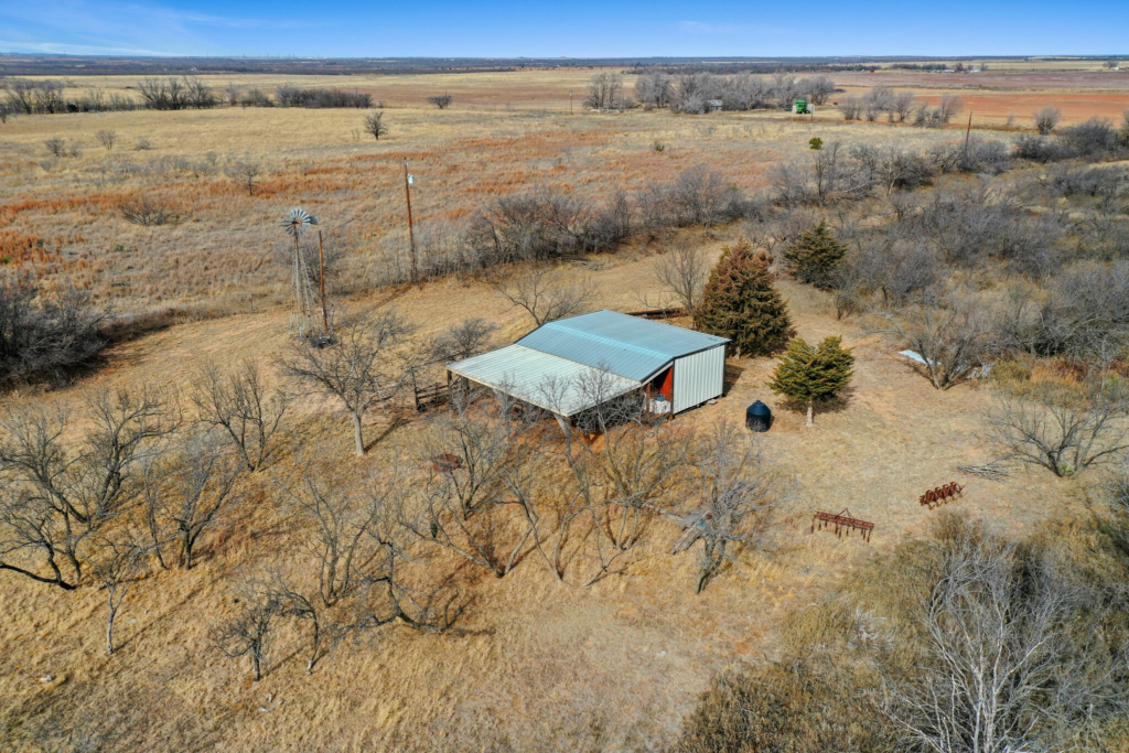 Aerial view of a metal-roofed cabin, windmill, and winter brush on the 80 acre property on Co Rd 228 near Afton, TX